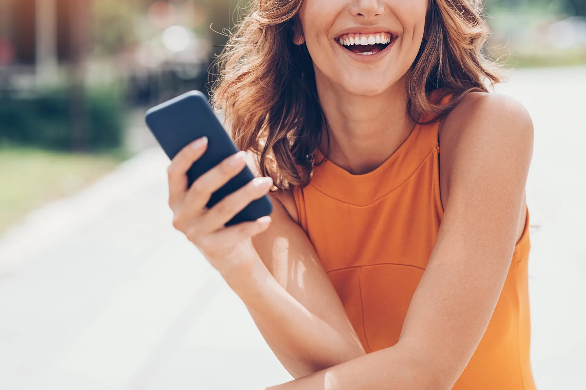 Donna sorridente con vestito arancione che tiene in mano uno smartphone.